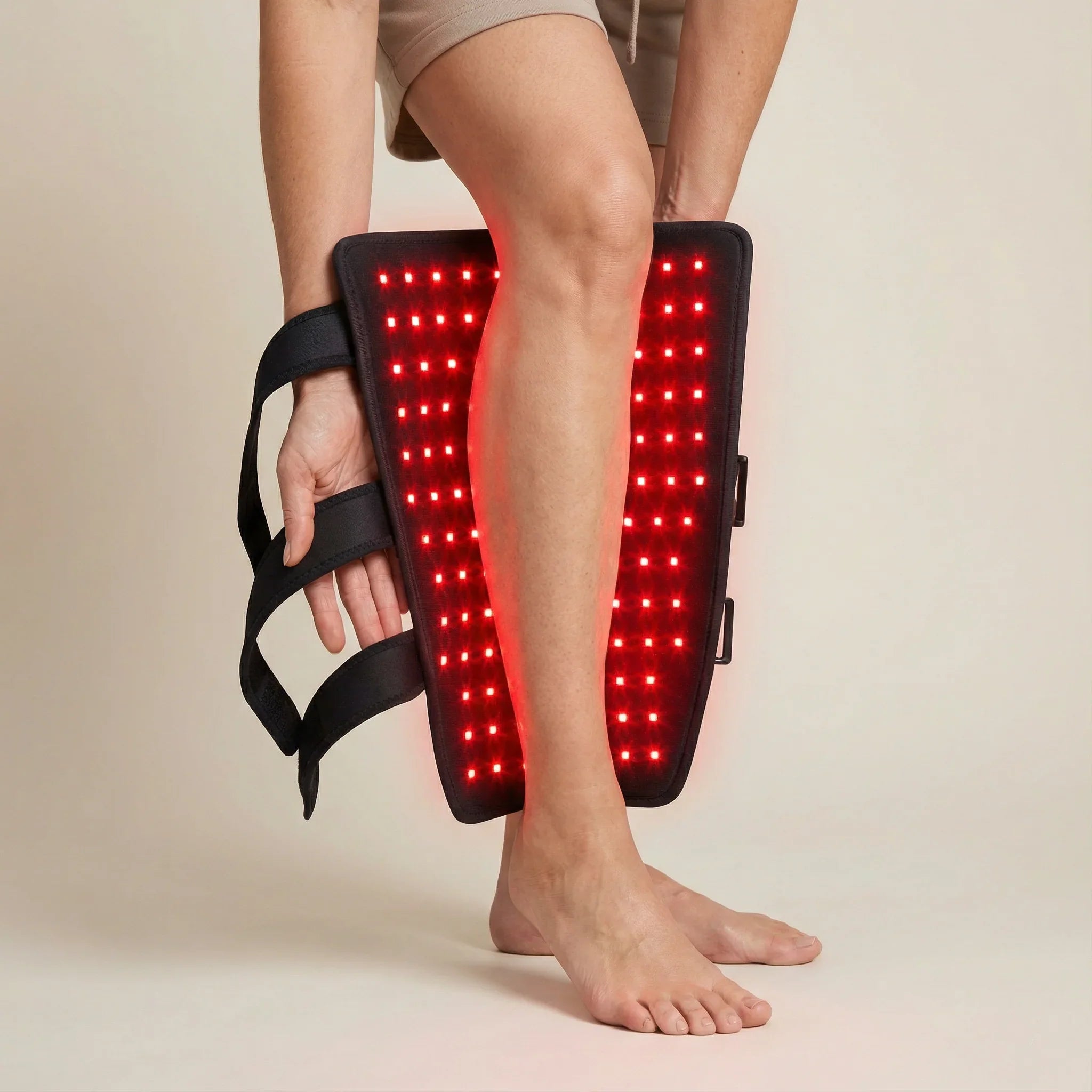 Person using a red light therapy device on their leg against a neutral background