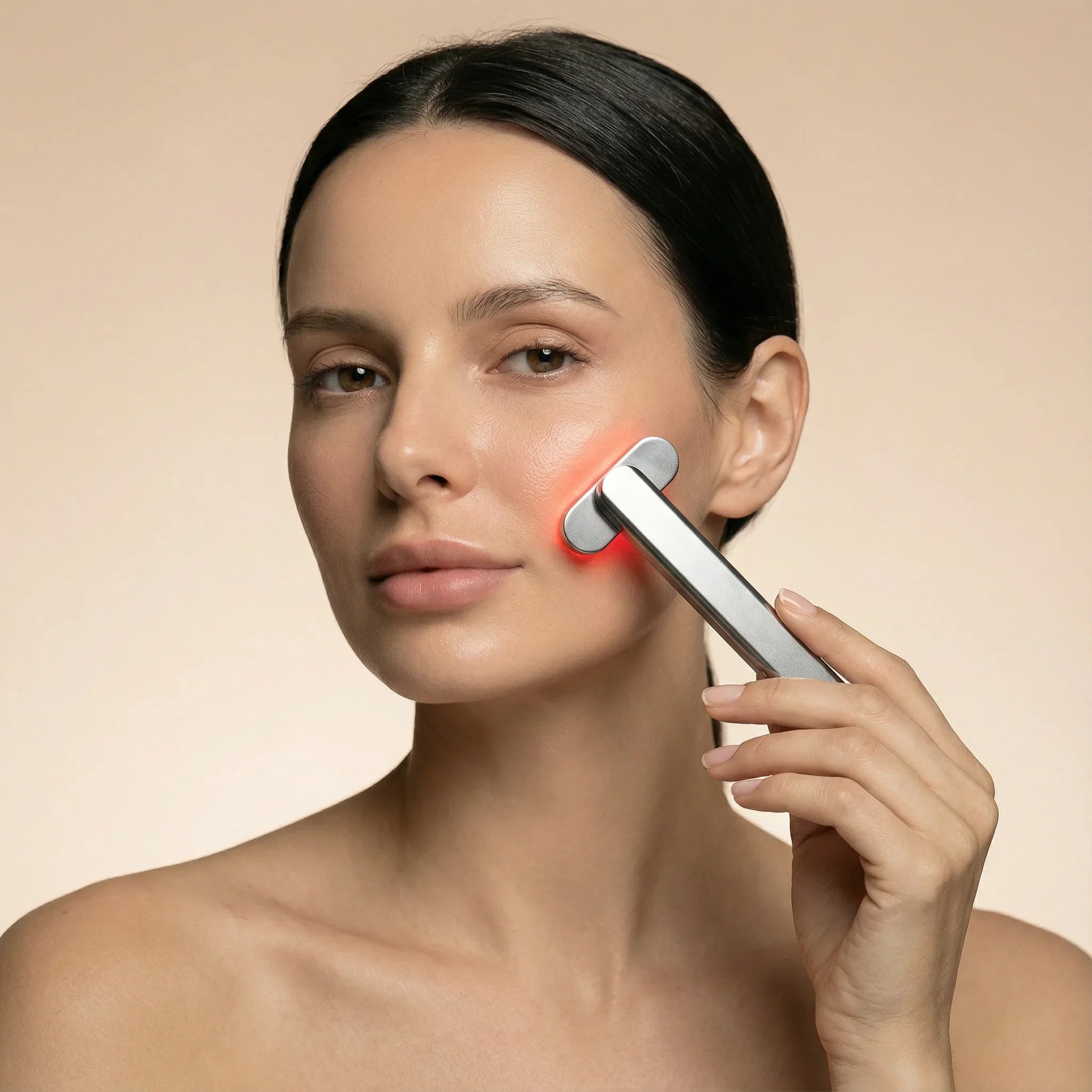 Woman using Nicebeam red light skin care device on her face against a beige background