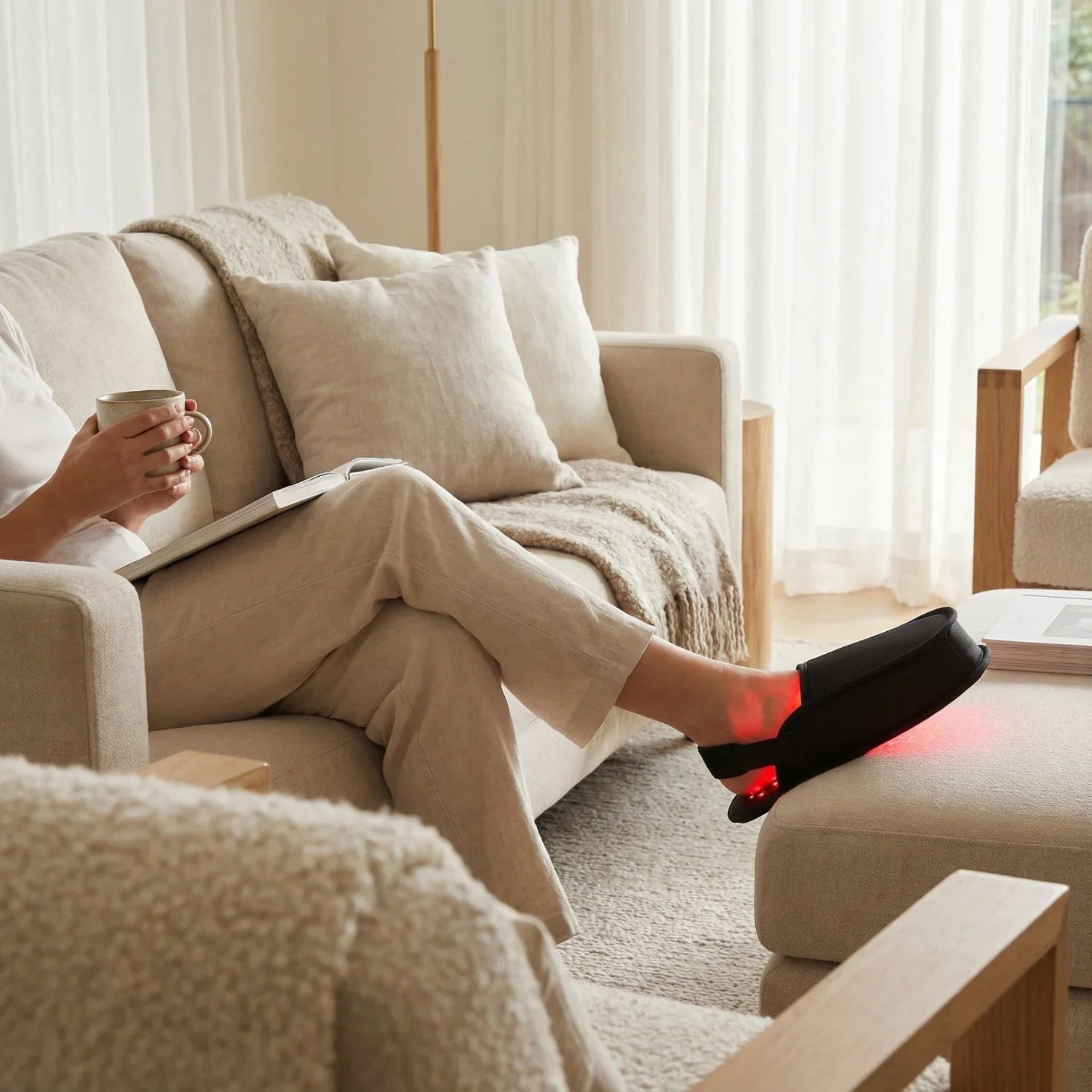 Person sitting on a couch with a cup and tablet, wearing Nicebeam black slippers with red lights.