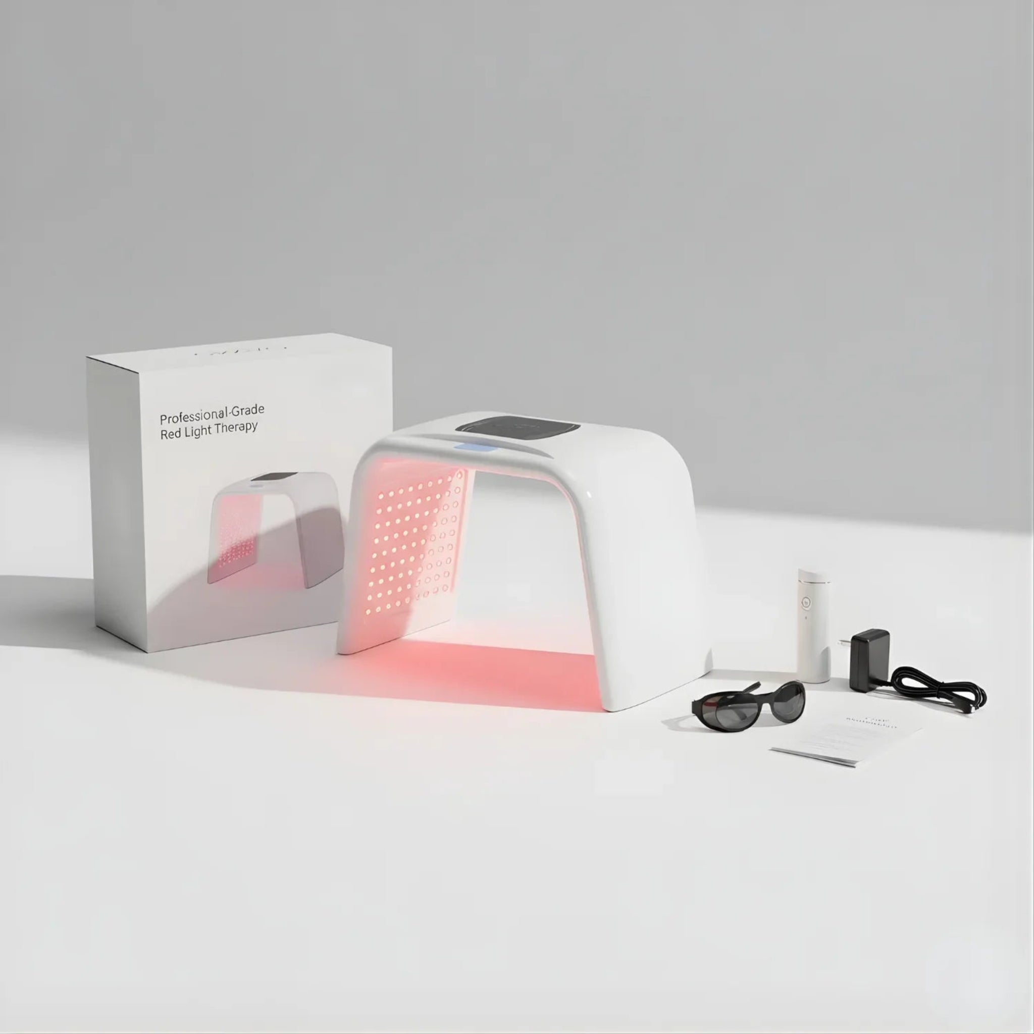 White light therapy device with red light, sunglasses, and power adapter on a gray background