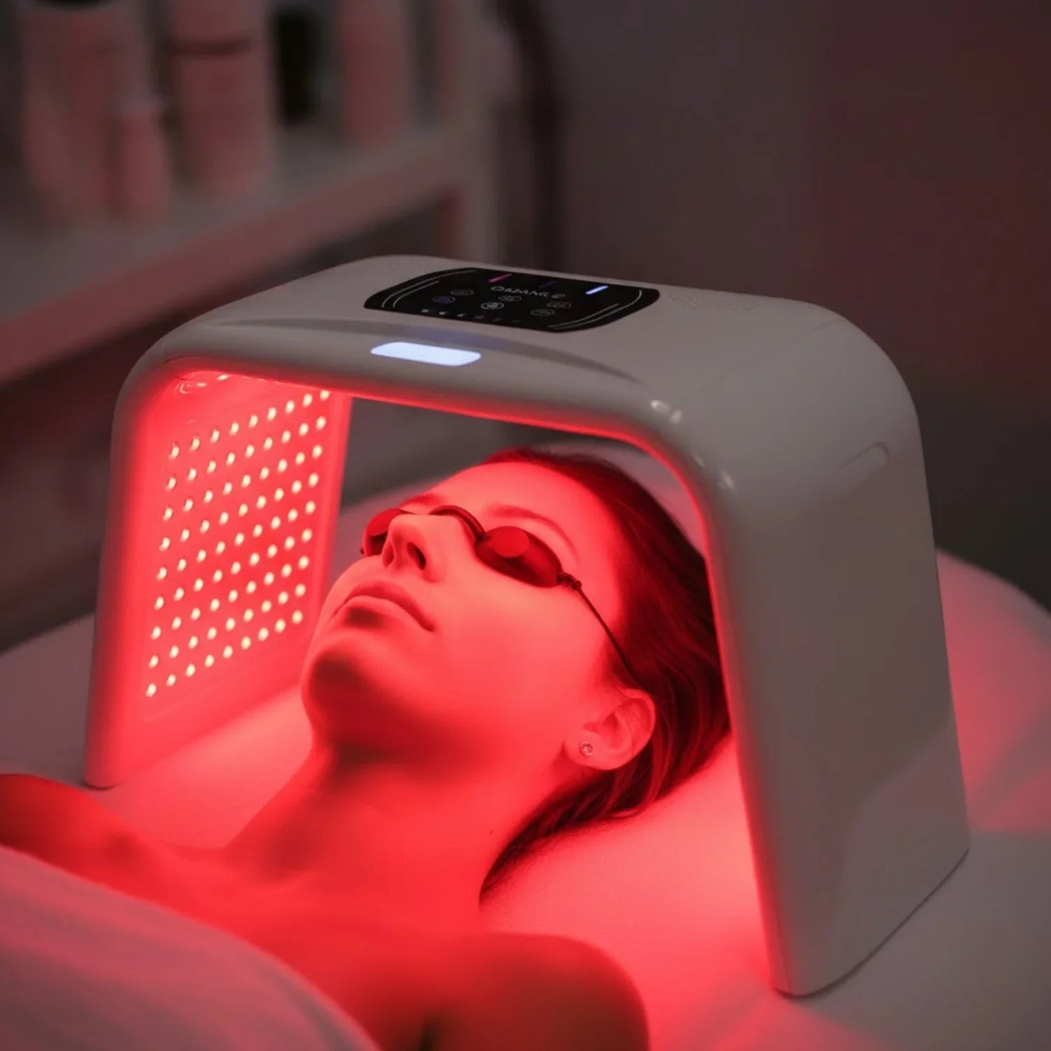 Person receiving red light therapy under a device with a blurred background
